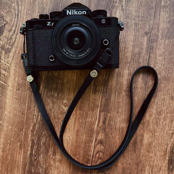Black Nikon camera with a full-grain leather strap on a wooden surface