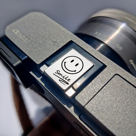 Vintage camera with a smiley face hot shoe cover labeled 'smile' on a blurred background