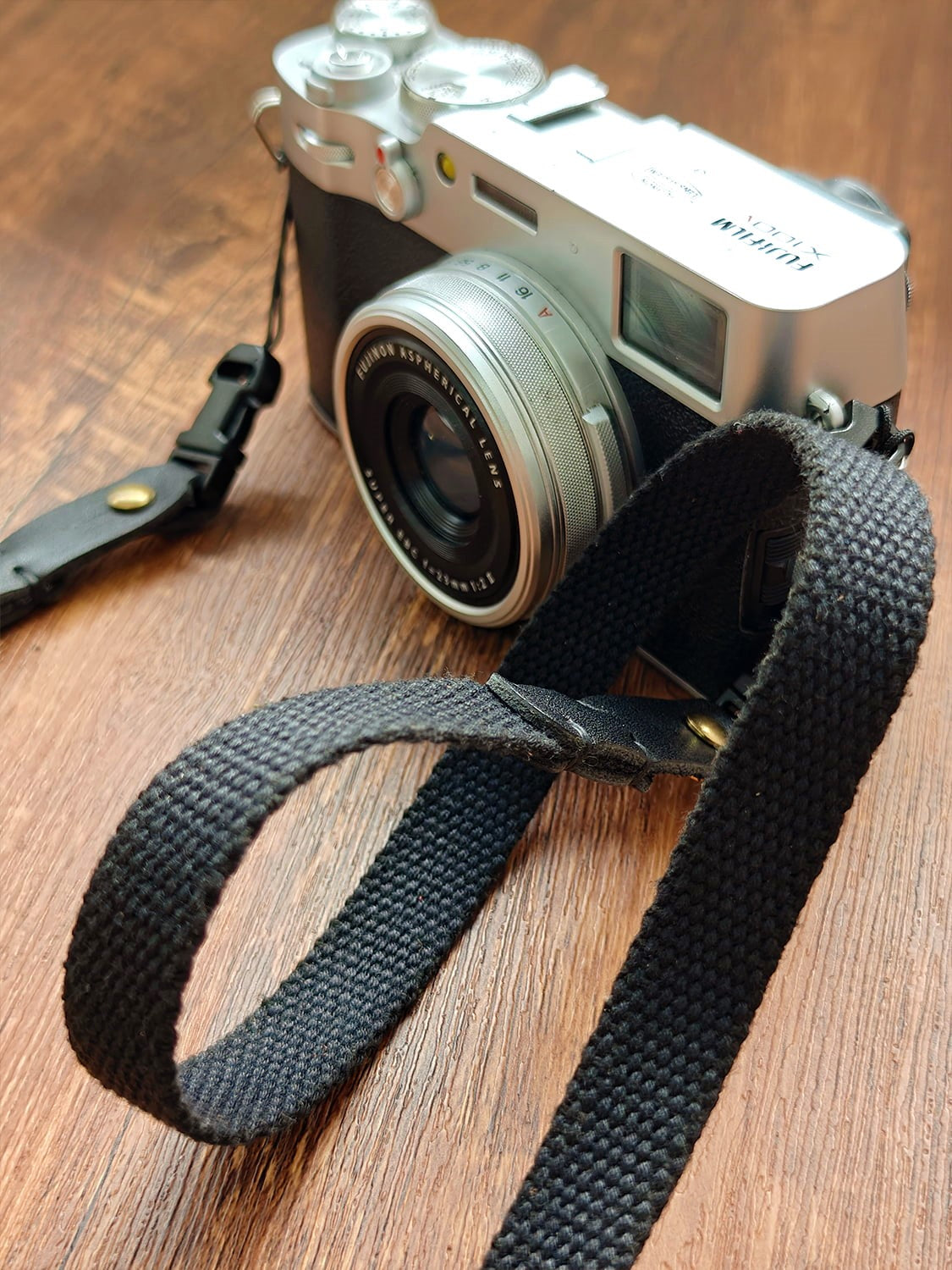 A camera with a black canvas strap on a wooden surface