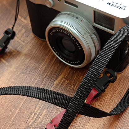 Black canvas camera strap with red leather connectors and quick-release buckle