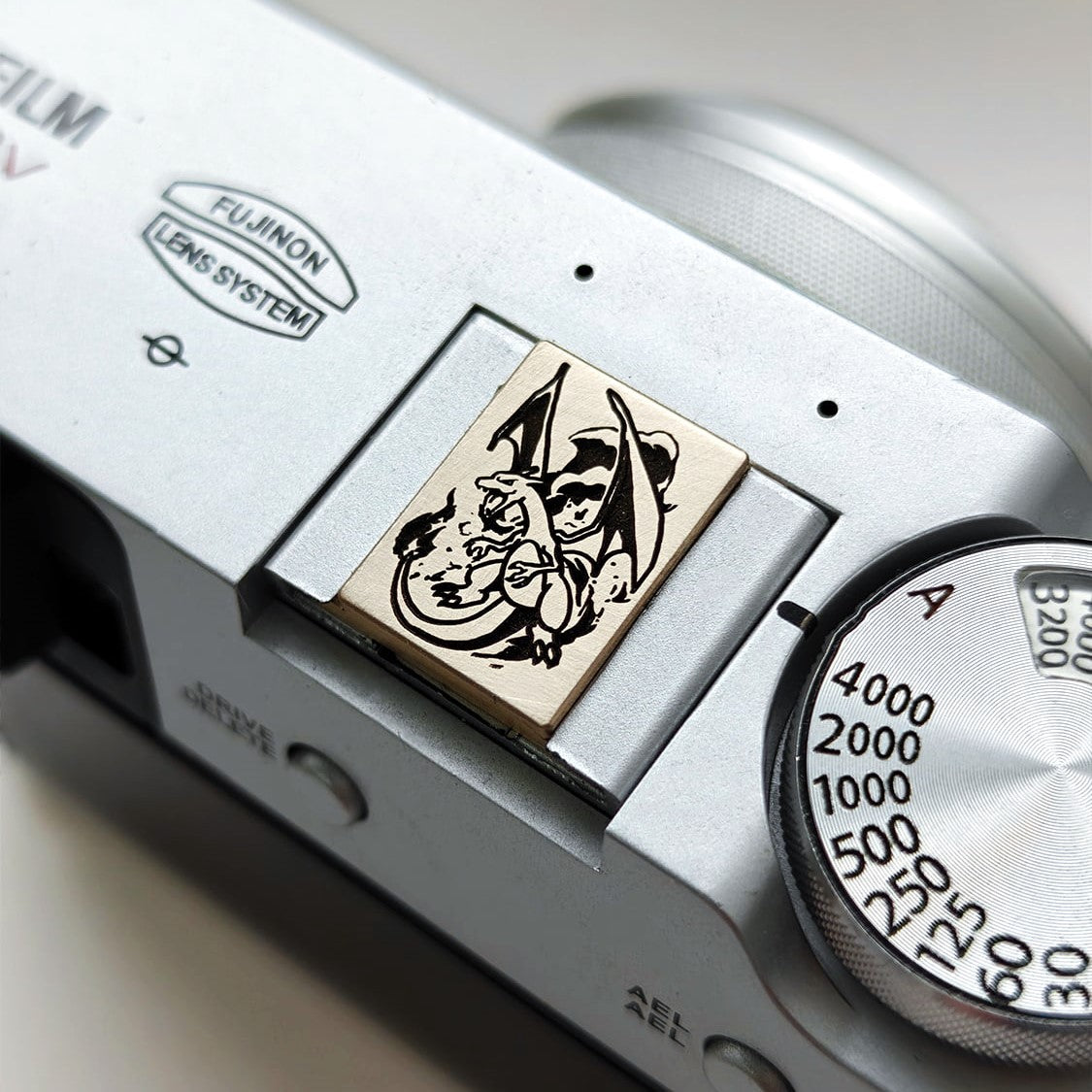 Charizard gold brass hot shoe cover on Fujifilm camera - front view