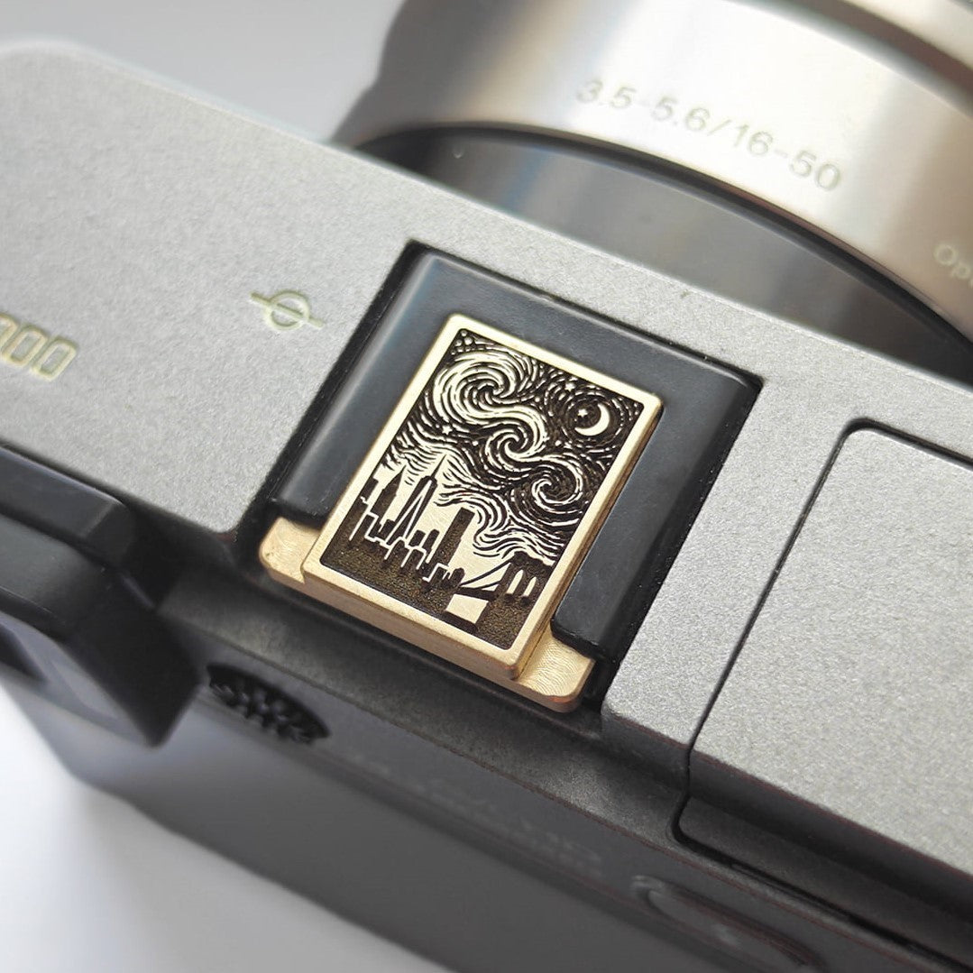 A close-up of a camera body featuring a hot shoe cover with the New York skyline and starry sky design.