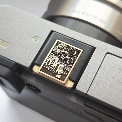 A close-up of a camera body featuring a hot shoe cover with the New York skyline and starry sky design.