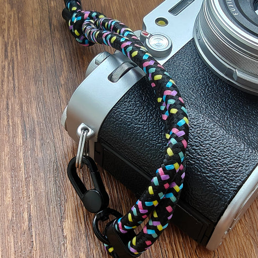 Camera with a colorful paracord strap on a wooden surface