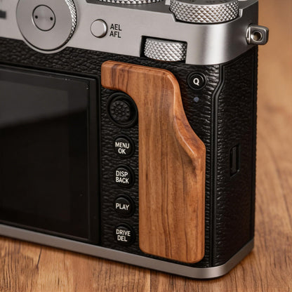 Close-up of the grip of a Fuji GFX100RF camera on a wooden surface.
