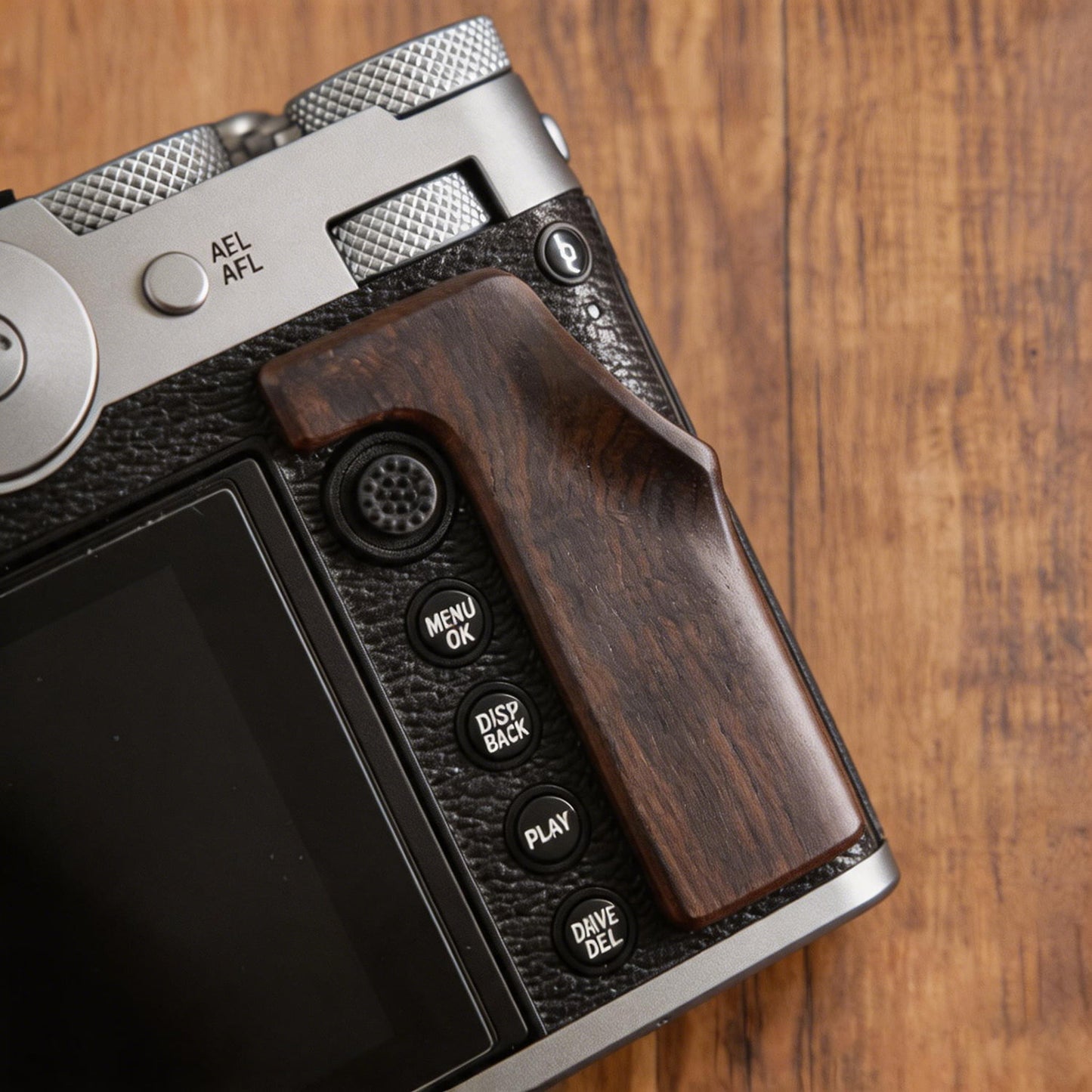 A close-up of a Fuji GFX100RF camera body with a dark brown wooden grip attachment, resting on a wooden surface. 