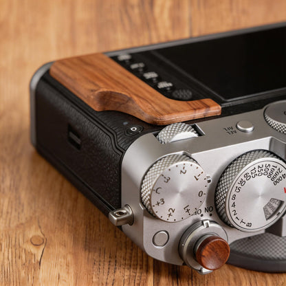 A close-up of a Fuji GFX100RF camera body with wood grip resting on a wooden surface.