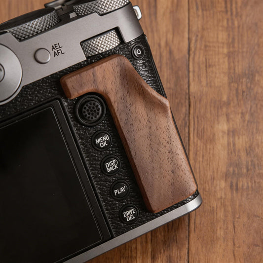 A close-up of a Fuji GFX100RF camera grip set against a wooden tabletop background.