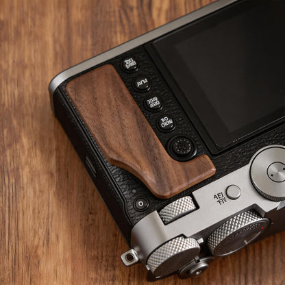 Close-up of a Fuji GFX100RF camera body with a dark brown wooden grip on the back.