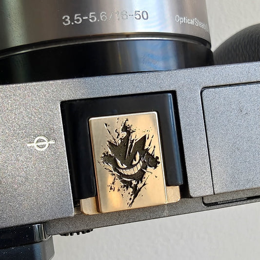 Close-up of a camera brass hot shoe cover with gengar design