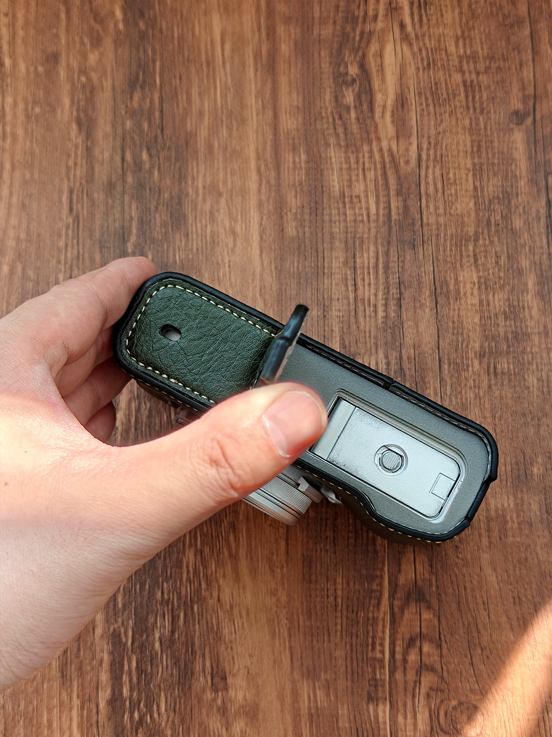 Hand holding a Fujifilm X100vi camera with a leather strap on a wooden surface