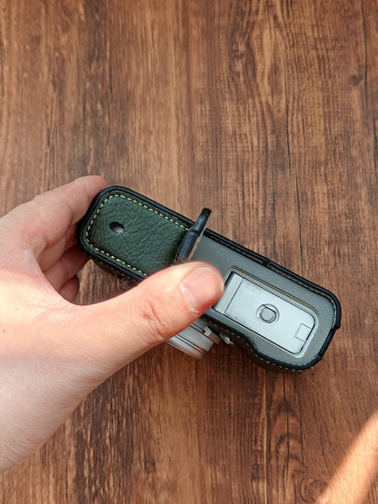 Hand holding a Fujifilm X100vi camera with a leather strap on a wooden surface