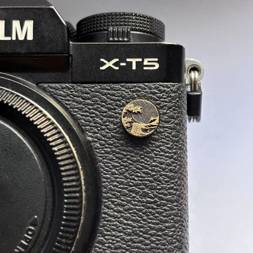 Close-up of a ocean wave design flash pc sync terminal cap cover on a black Fujifilm X-T5 camera
