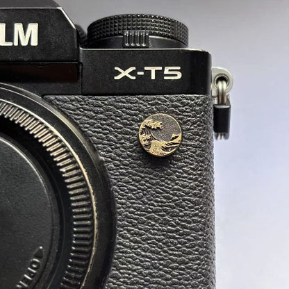 Close-up of a ocean wave design flash pc sync terminal cap cover on a black Fujifilm X-T5 camera
