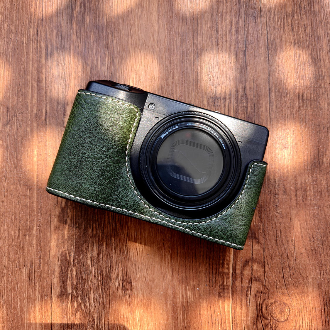 Ricoh GR3 camera with a green leather case on a wooden surface