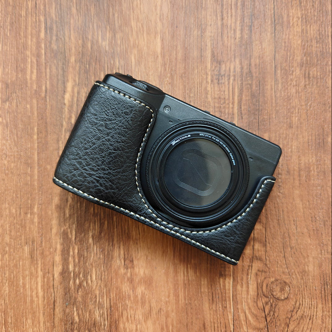 Black Ricoh GR III camera with leather case on a wooden surface