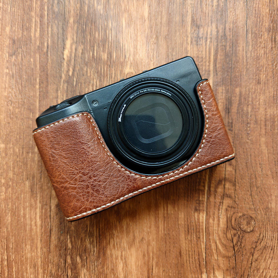 Ricoh GR III camera with a brown leather case on a wooden surface