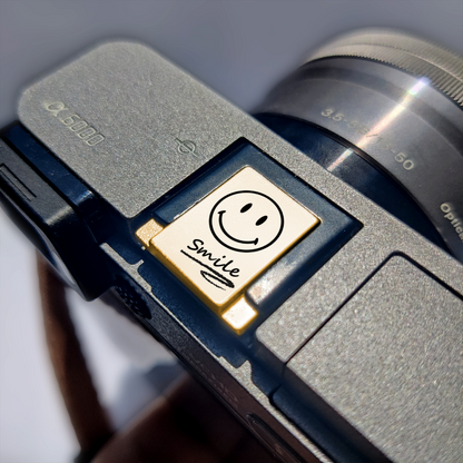 a smiley face hot shoe cover labeled 'smile' on sony camera