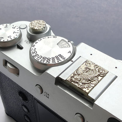 Close-up of a Fujifilm camera with a decorative hot shoe cover and shutter button on a gray background