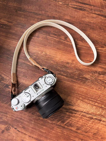 Camera with white canvas strap on a wooden surface