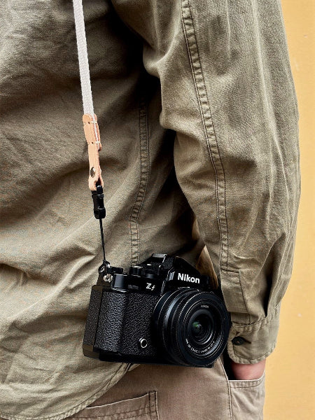 Person wearing a Nikon camera on a white canvas leather strap 